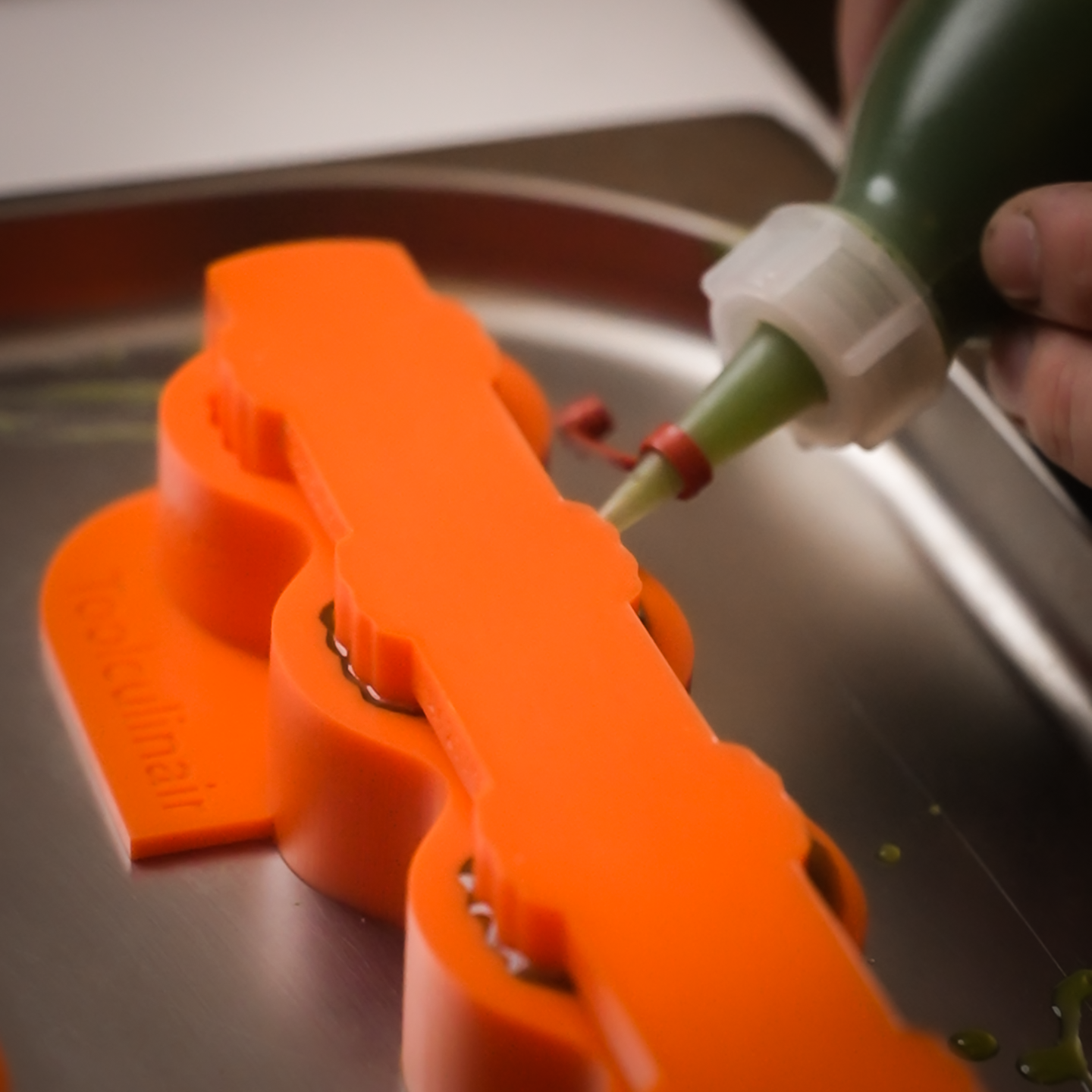 Spray bottle filled with green liquid filling an artichoke mold on a baking tray during mise en place preparation.