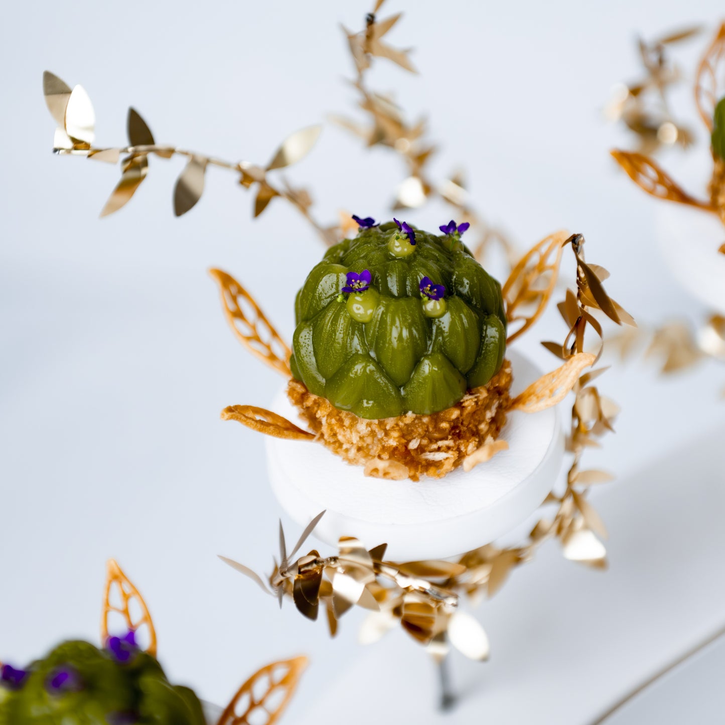 Angled side-top view of an artichoke-shaped piece presented on a pillar, with other artichoke pieces partially visible in the background, created by Bocuse d’Or Netherlands for fine dining presentation.