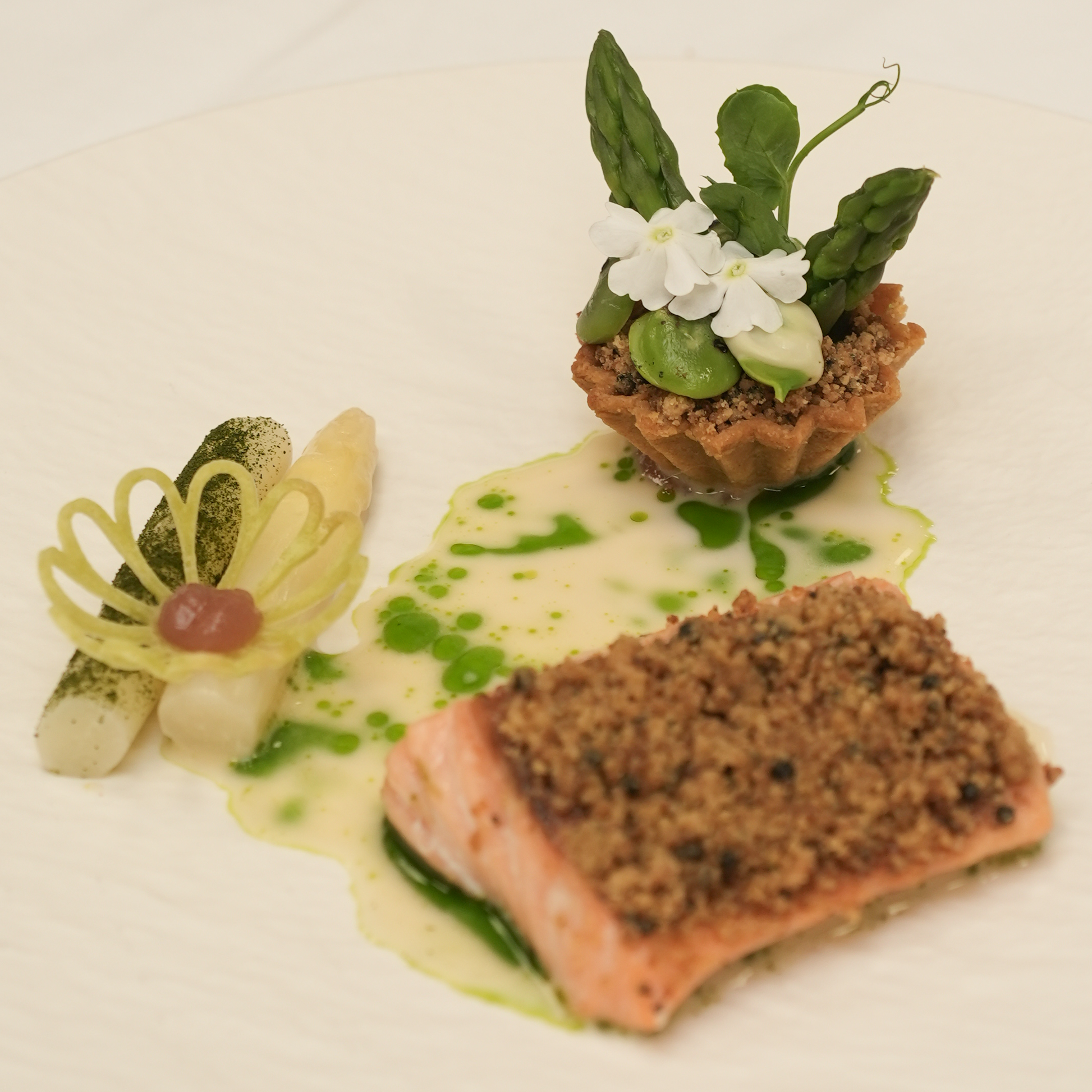 Fine dining dish created by ROC Sterklas students featuring asparagus, baked salmon, a cream-filled tartelette and a tuile placed on top of the asparagus.
