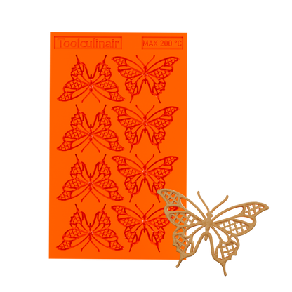 3D render of an orange Toolculinair silicone butterfly tuile mold with visible logo, showing a decorative butterfly-shaped tuile with elegant wing patterns in the bottom right corner as the finished result.