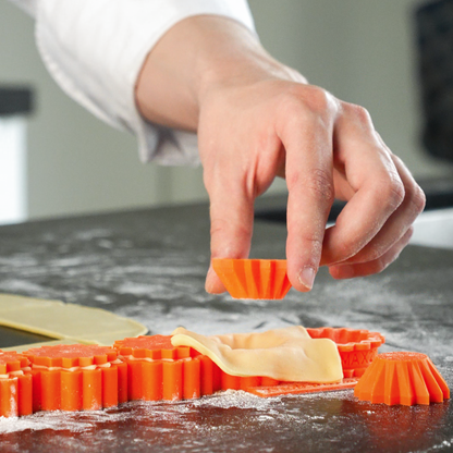 Close up photo of a hand holding and using a crimped silicone tartelette cap  flexible and food safe tool for shaping perfect pastry edges.
