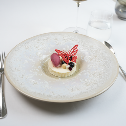 Atmospheric dessert presentation at The Moerbei by Michael Corpel, featuring a plated dessert topped with a red butterfly tuile, served with wine glass and cutlery in a fine dining table setting