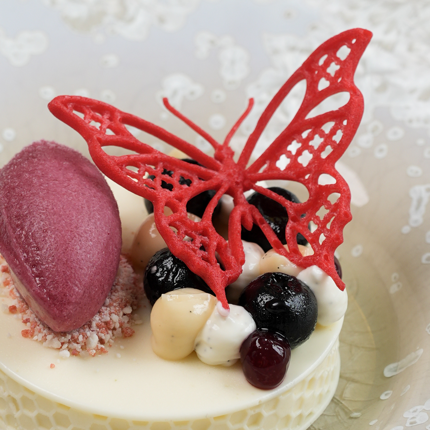 Close-up dessert plated at The Moerbei by Michael Corpel, topped with a red butterfly tuile, shown in detail with focus on the tuile garnish.
