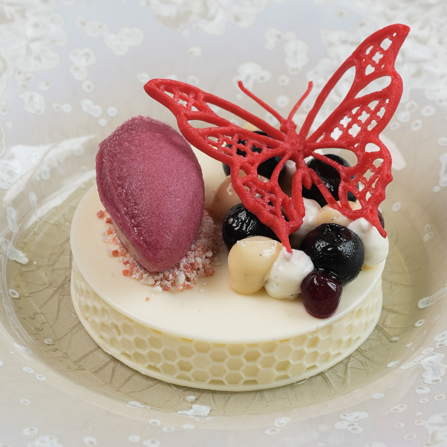 Dessert plated at de Moerbei by Michael Corpel, topped with a red butterfly tuile, shown in a wider composition of the full dish presentation.
