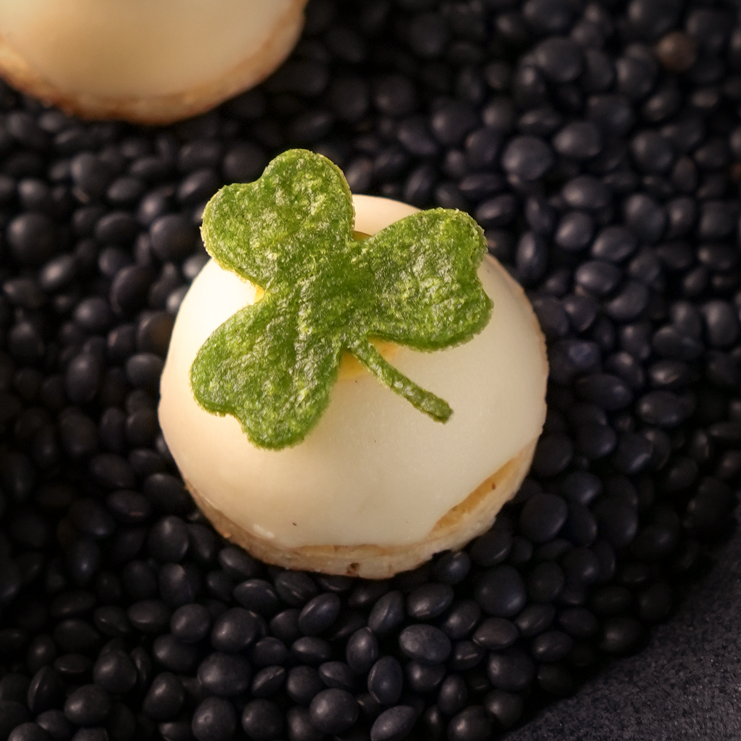 Spinach tuile shaped like a clover, elegantly presented on an amuse.